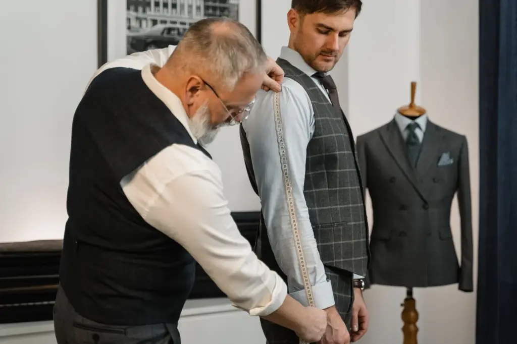 A tailor fitting a made-to-measure jacket with ready-made suits displayed behind