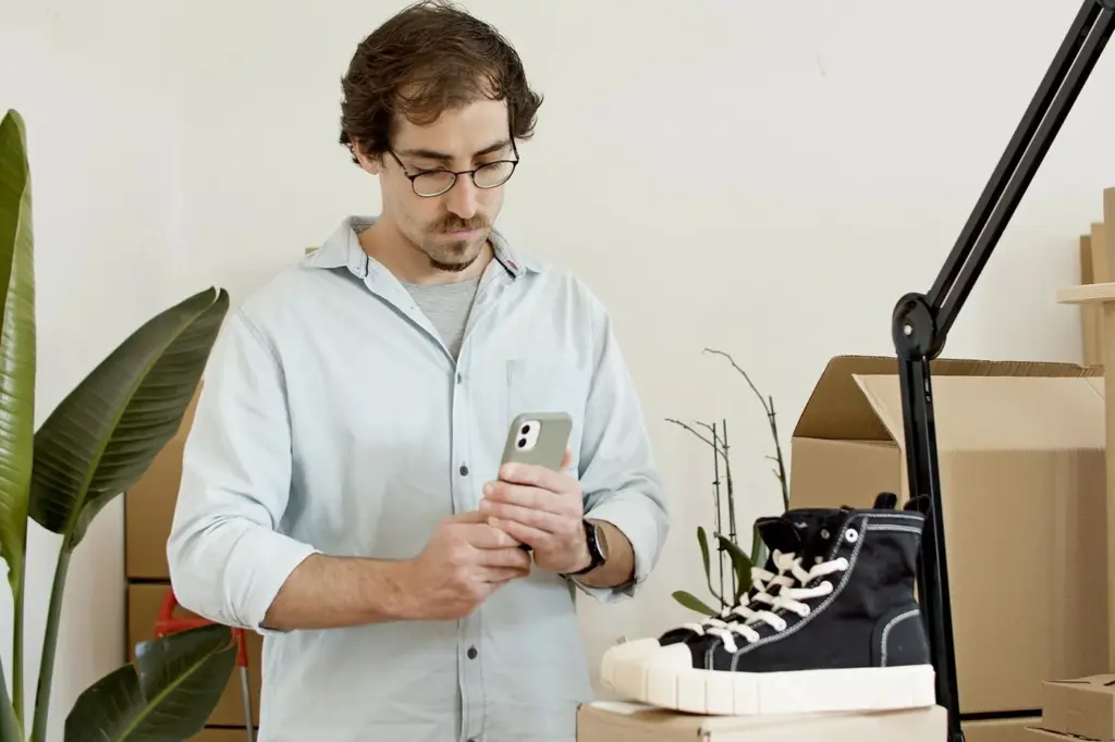 A seller photographing a pair of shoes with a phone at a desk