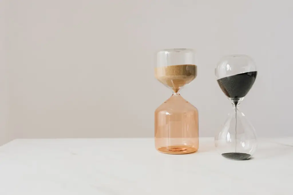 Two hourglasses standing side by side on a pale surface