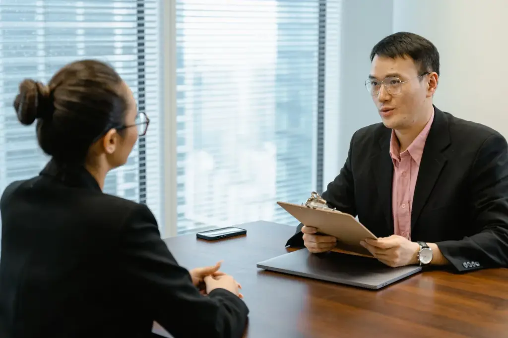 Two professionals talking across a desk in a bright office meeting