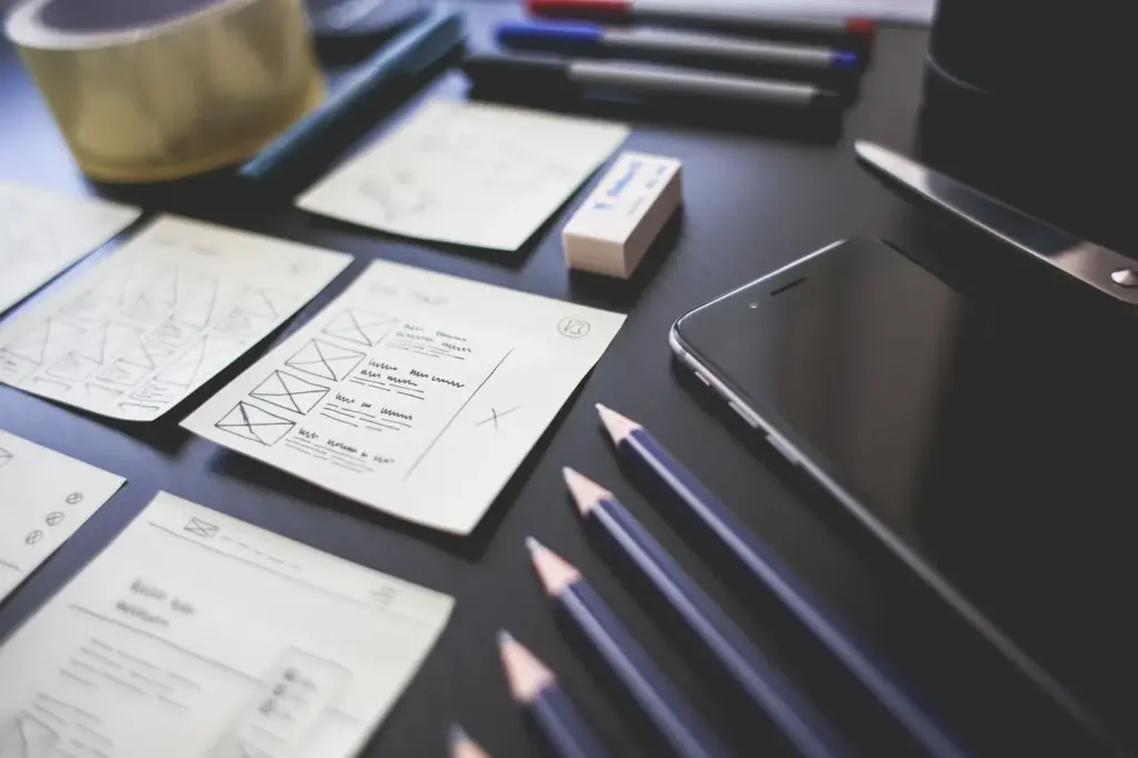 Hand-drawn page layout cards spread across a dark desk beside pencils
