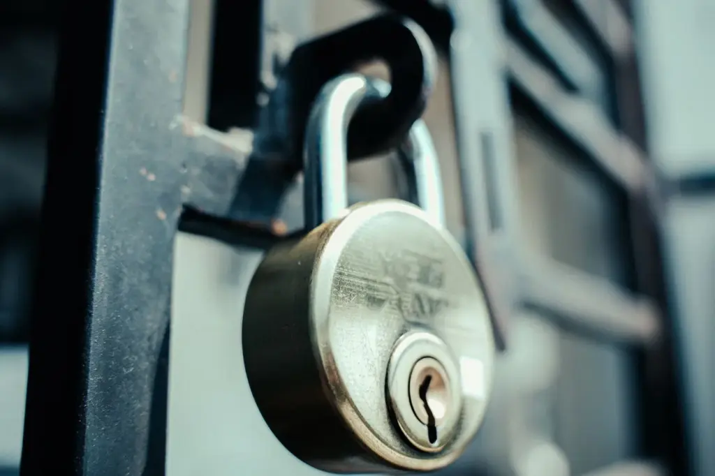 A brass padlock securing a metal gate