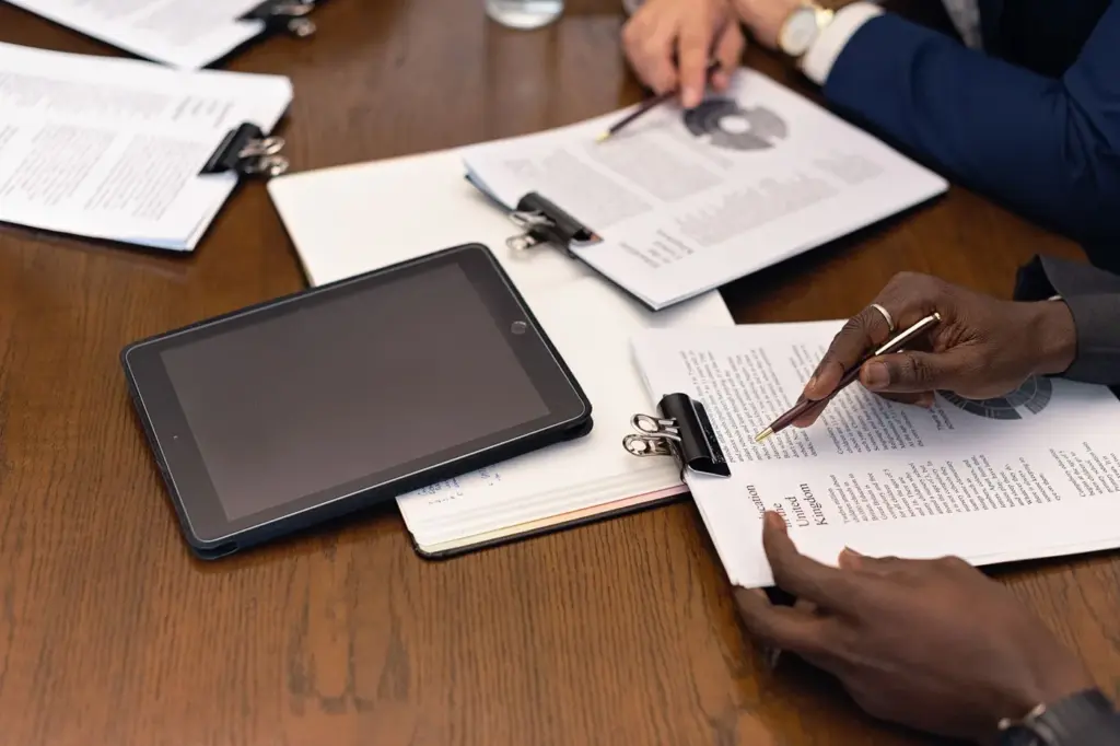 People reviewing printed documents and a tablet across a meeting table